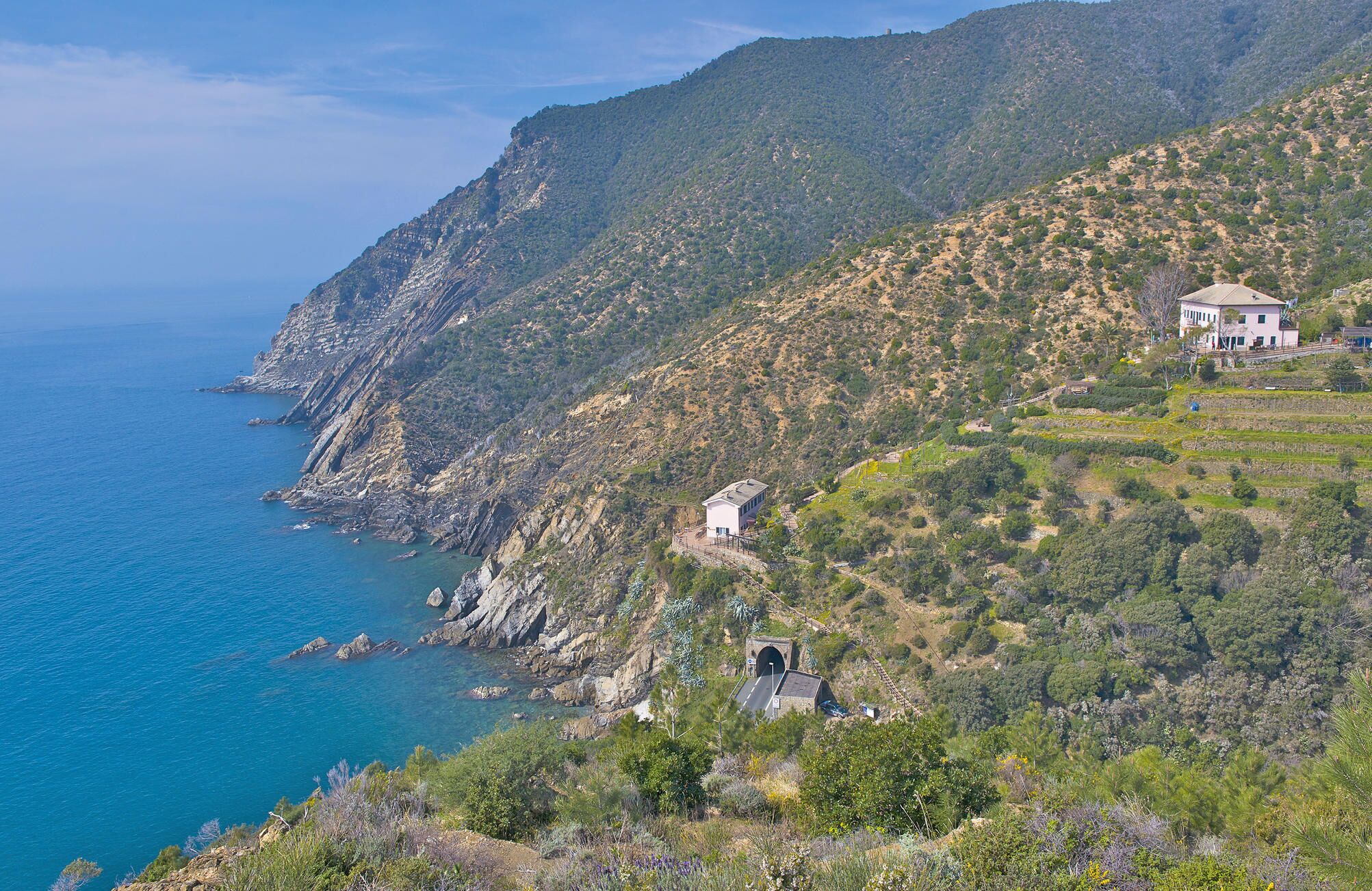 A coastal landscape with a mountain, a small building, and a road leading to a tunnel.