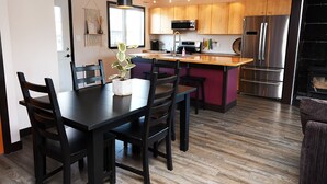 A modern kitchen with wooden cabinets, a stainless steel refrigerator, and a dining area with a black table and chairs.