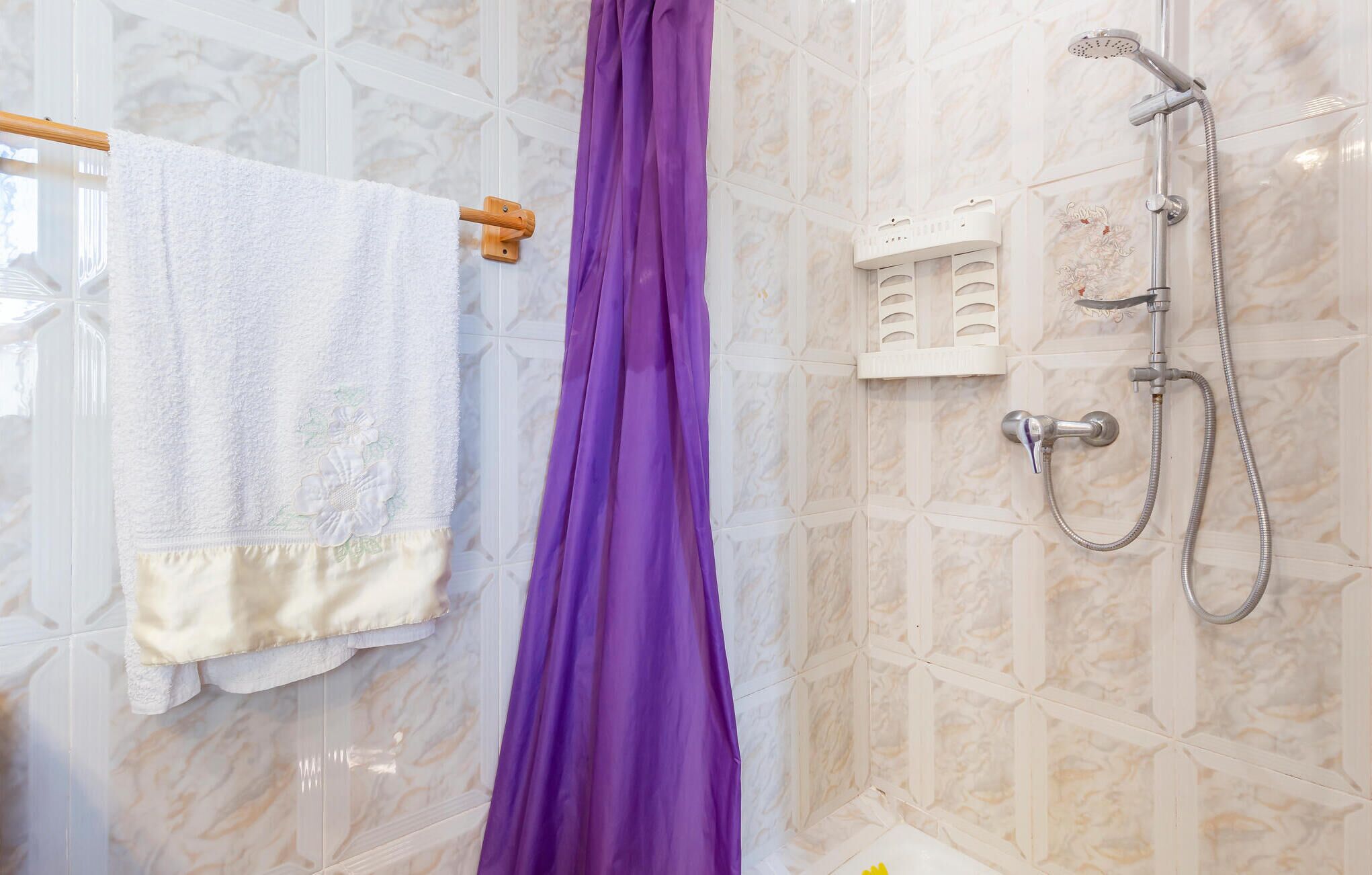 A bathroom with a shower, a towel rack with a white towel, and a purple shower curtain.