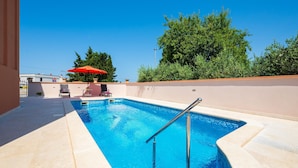 Una piscina con una scala in metallo, circondata da un muro beige e un ombrellone rosso.