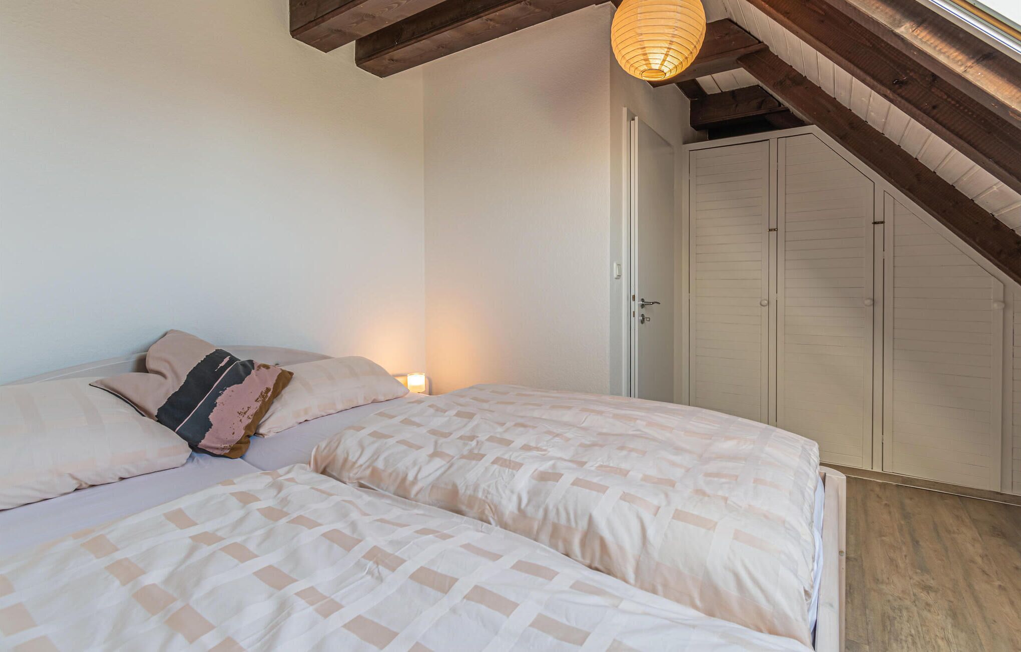 Une chambre avec deux lits, un plafond en bois, une armoire blanche et un luminaire suspendu.