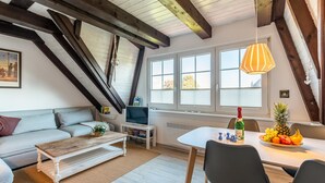Een loft-achtige kamer met een bank, een houten salontafel, een eettafel met stoelen, een televisie en een fles champagne.