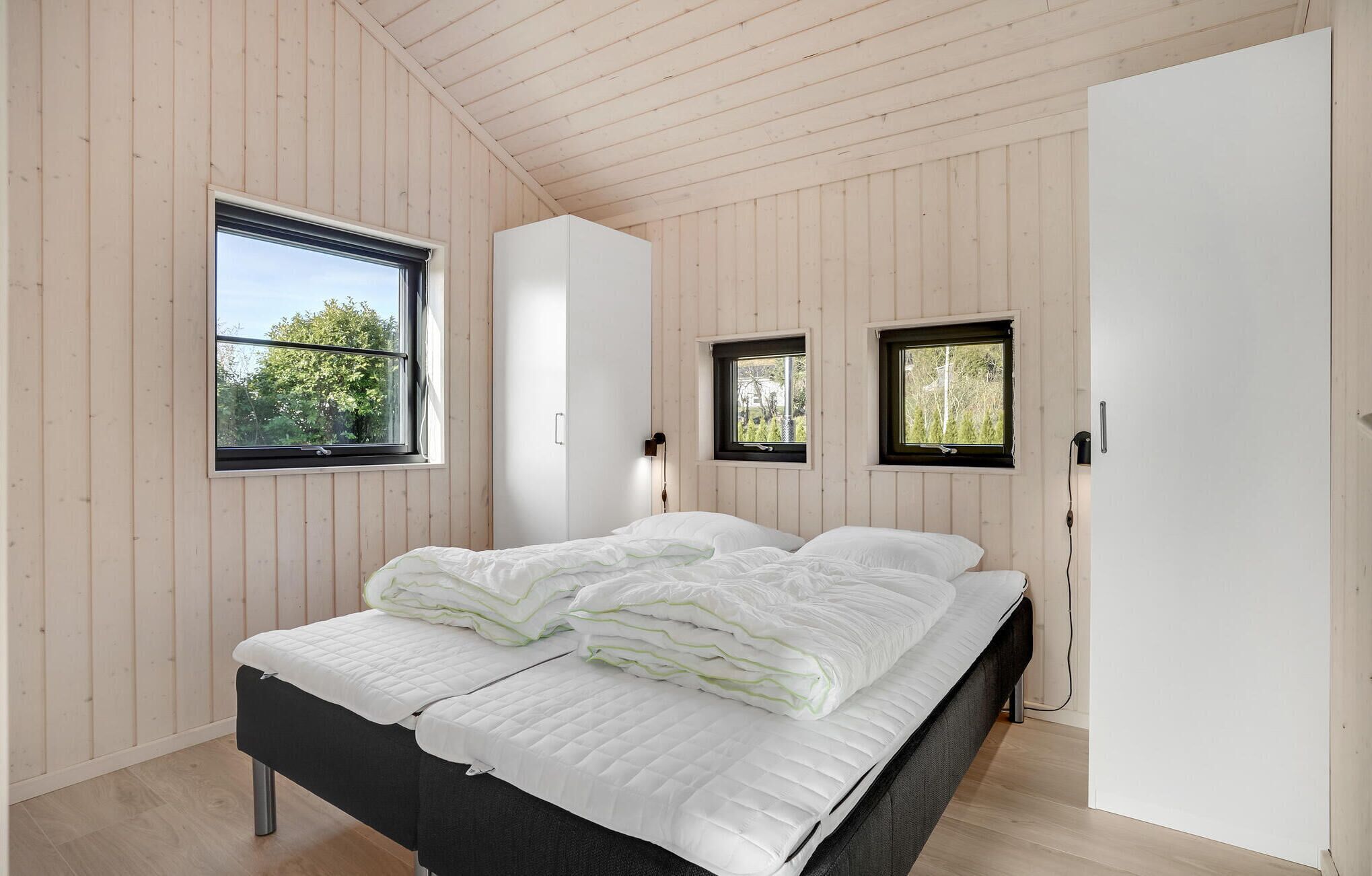 A bedroom with a bed, two windows, a wardrobe, and a door.