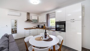 A modern kitchen with white cabinets, a built-in oven, and a dining area with a round table and chairs. - Awesome apartment in Obrovac (Obrovac)
