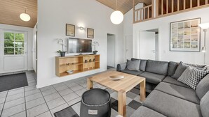 Un salon moderne avec un canapé gris, une table basse en bois et un téléviseur posé sur une étagère en bois. Un escalier mène à un niveau supérieur.