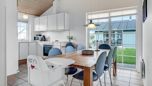 Une cuisine moderne avec des meubles blancs, une table à manger en bois et des chaises bleues. Une grande fenêtre offre une vue sur l’extérieur.