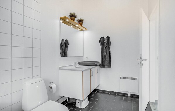 Un baño moderno con inodoro, lavabo y espejo. Hay toallas colgadas en la pared y un radiador debajo del lavabo.
