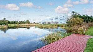 Une vue paisible sur un lac, avec un bâtiment moderne en verre, une jetée en bois et une végétation luxuriante tout autour.
