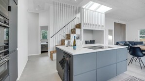 A modern kitchen with a central island, built-in appliances, and a dining area with a blue chair. - 4 bedroom gorgeous home in Esbjerg V (Esbjerg V)