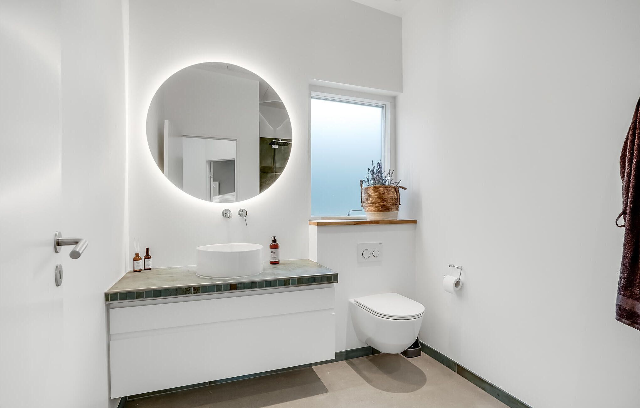 Une salle de bain moderne avec un miroir rond, un lavabo blanc et des toilettes.