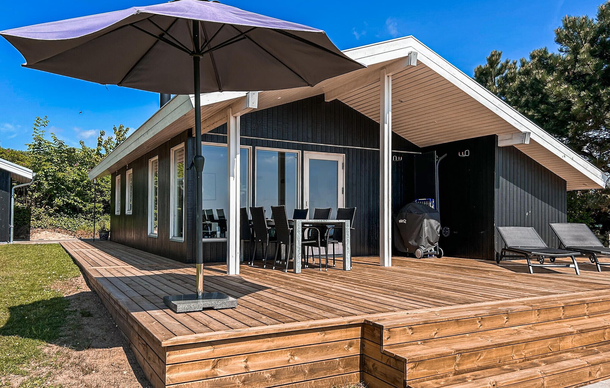 A modern wooden cabin with a deck, outdoor seating, and a covered patio area.