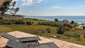 A wooden deck with lounge chairs overlooking a coastal landscape with a house and a view of the sea. - Awesome home in Faaborg with WiFi (Faaborg)