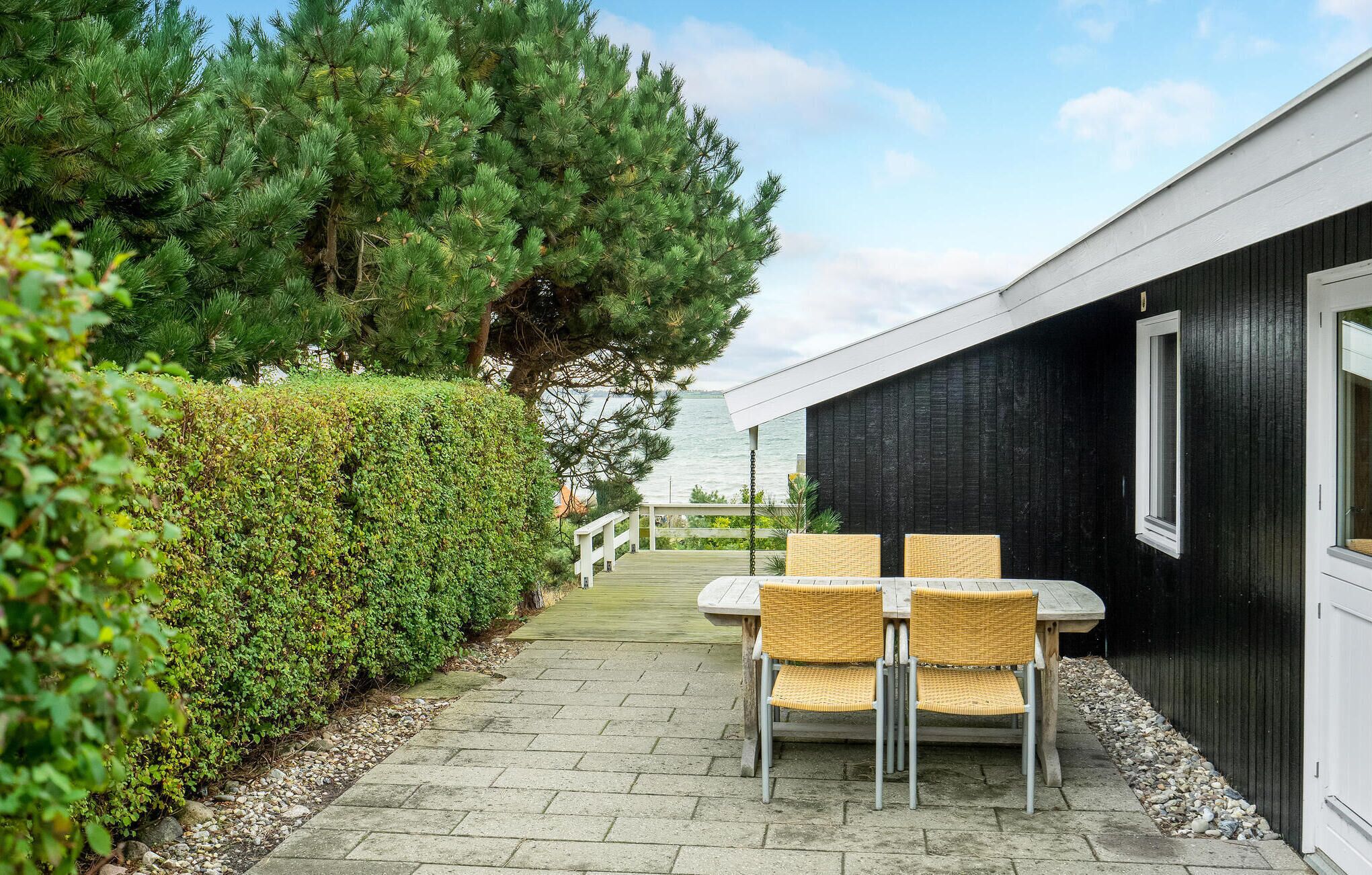 A patio with a table and chairs, a hedge, and a view of the water.