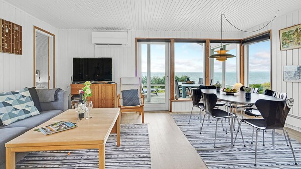 A modern living room with a sofa, coffee table, and TV. It features a dining area with chairs and a table, large windows with a view of the sea, and a wooden ceiling. - Awesome home in Faaborg with WiFi (Faaborg)