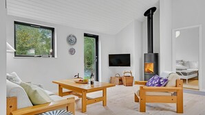 Una sala de estar moderna con chimenea, muebles de madera, televisor y vista a zonas verdes.