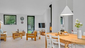 Una sala de estar moderna con una mesa de comedor de madera, sillas blancas, un ventanal grande y una chimenea.