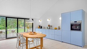 Una cocina moderna con una mesa y sillas de madera, armarios azul claro y un ventanal con vistas a un jardín.