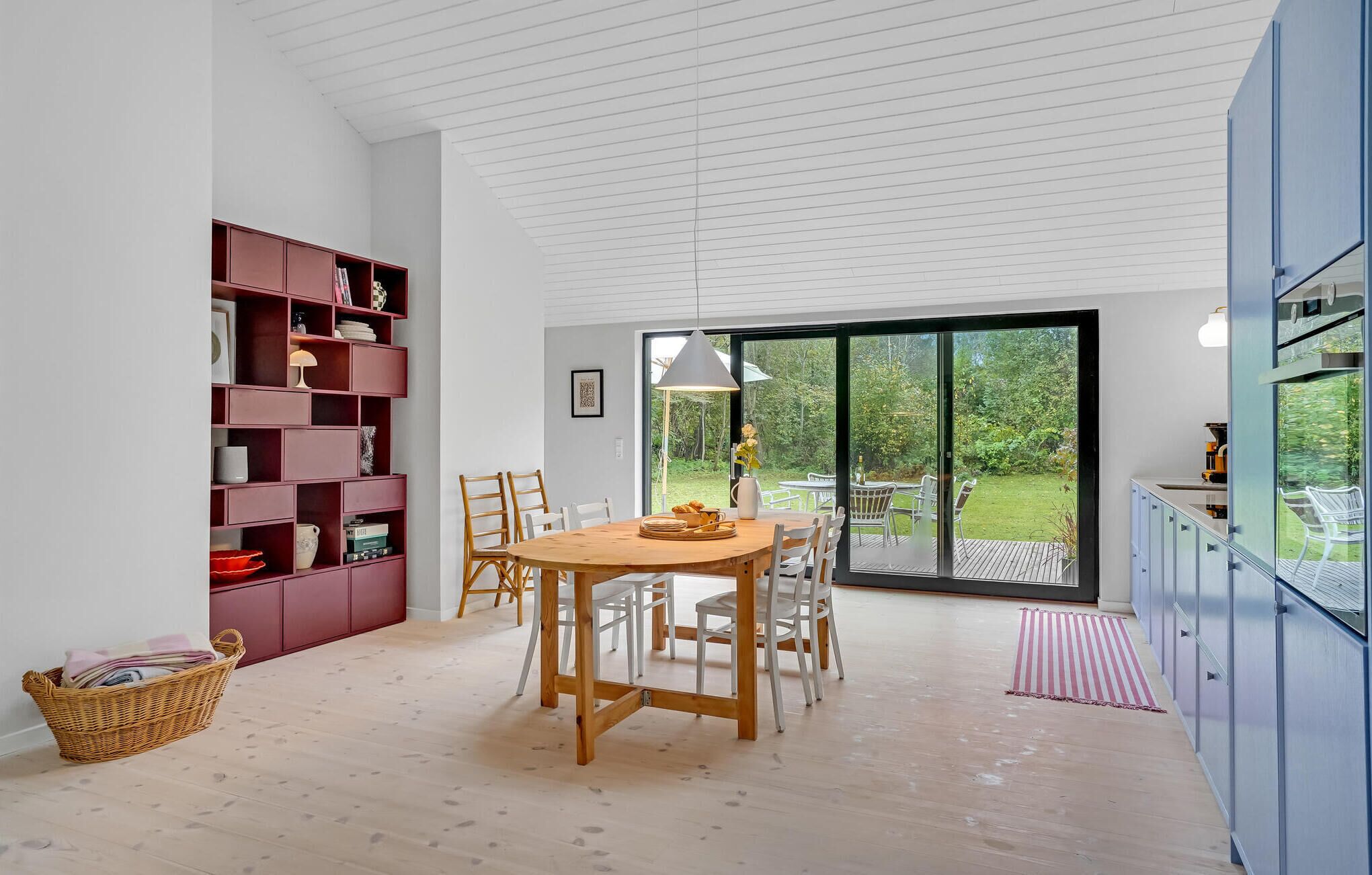 Une cuisine moderne avec un coin repas, comprenant une table en bois, des chaises et une grande fenêtre donnant sur un jardin.