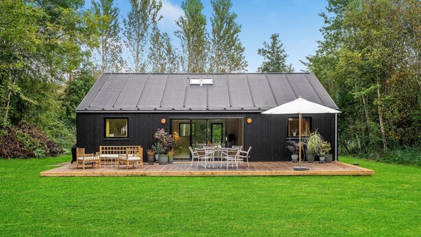 Una casa moderna negra con una terraza, mobiliario exterior y un paraguas grande.