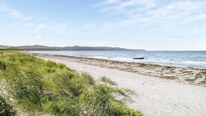Una playa con orilla arenosa, zonas con césped y un bote en el agua.