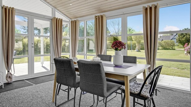 Un espace repas moderne, doté d’une table et de chaises, de grandes fenêtres et offrant une vue sur l’extérieur.