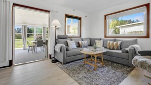 Un salon spacieux avec un canapé gris, une petite table basse en bois et un coin repas comprenant une table et des chaises.