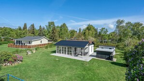 Une propriété résidentielle dotée d’une grande pelouse, d’un patio couvert et d’un petit bâtiment à la façade en verre.