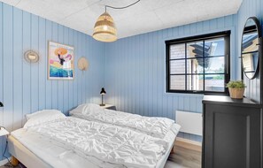 Une chambre à coucher avec un lit, des tables de chevet, un luminaire suspendu, une fenêtre et un miroir.