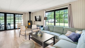 Een moderne woonkamer met een bank, fauteuils, een open haard en grote ramen.