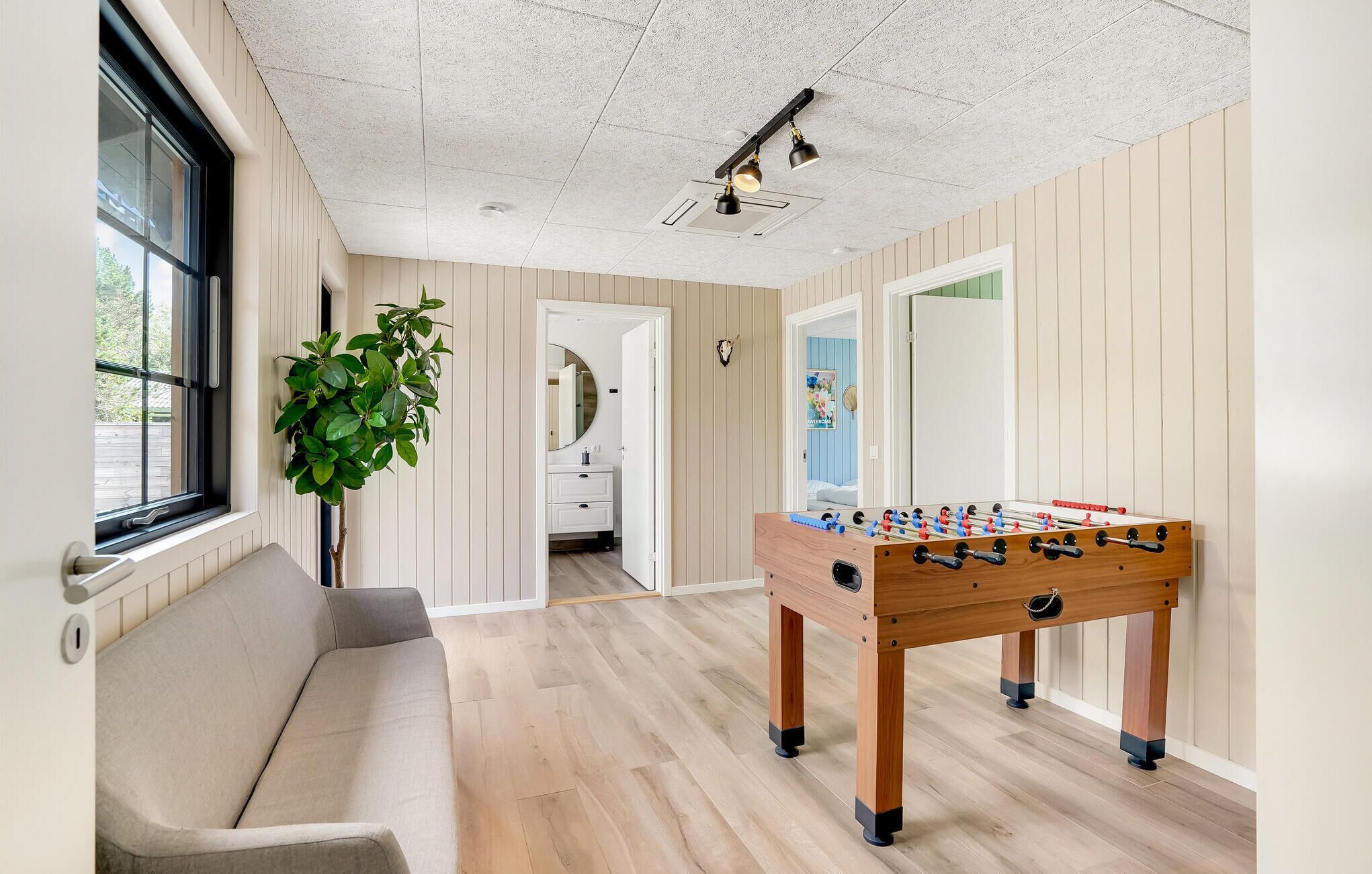 Een kamer met een bank, een tafelvoetbalspel, een plant en een spiegel.