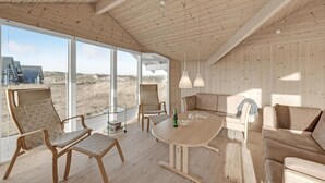 Una habitación amplia con una gran mesa de madera, dos sillas, un sofá y vistas a la playa a través de amplias ventanas.