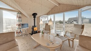 Un cuarto acogedor con techo de madera, chimenea, televisor y un amplio ventanal con vistas al exterior.