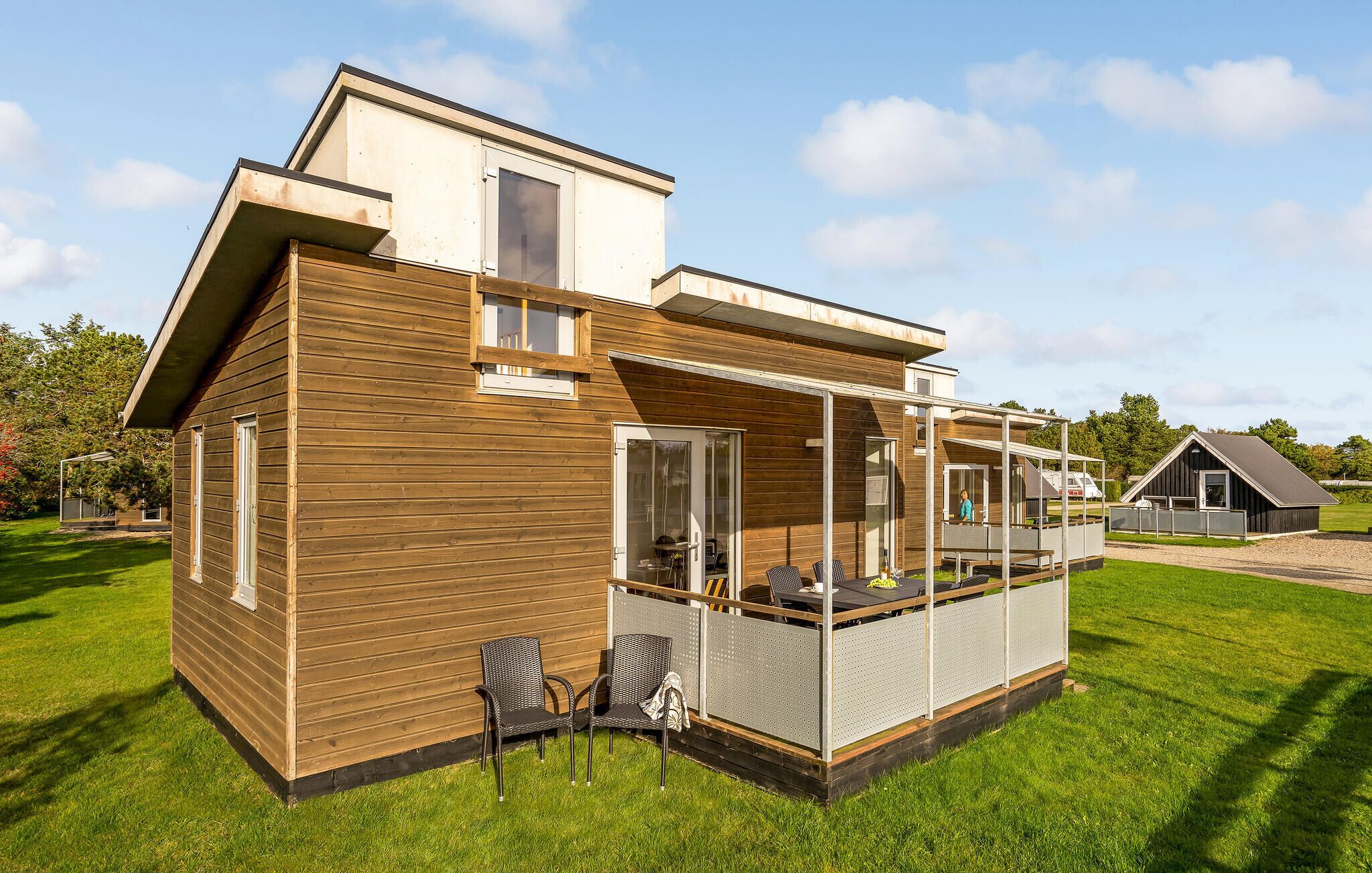 A modern wooden house with a balcony and a covered outdoor seating area.