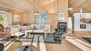 A modern interior with a wooden ceiling, a sofa, a black leather chair, a dining table, and a kitchen area.