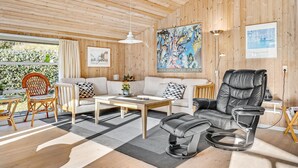 A cozy living room with a wooden ceiling, a sofa, a black leather chair, and a coffee table.