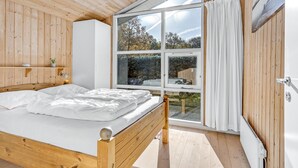 A bedroom with a wooden bed, a large window with curtains, and a white radiator.