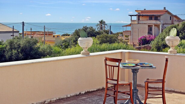 A terrace with two wooden chairs and a table, overlooking a coastal view with buildings and a clear sky. - Lovely home in Cava D'aliga with house sea view (Cava D'aliga)