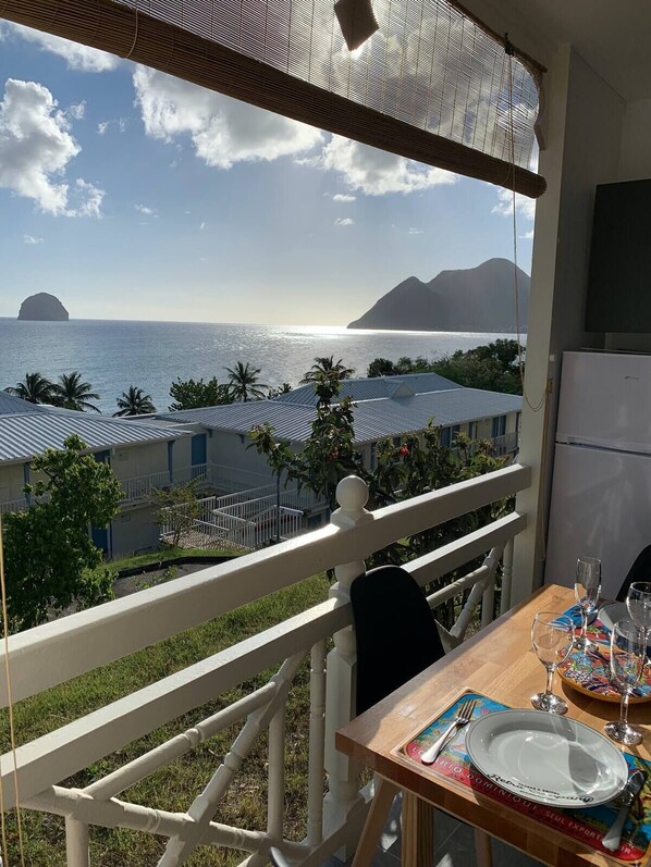 A balcony with a table set for dining, overlooking a coastal view with buildings and palm trees.