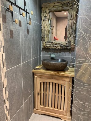 Un baño con lavabo de piedra, mueble de madera y espejo con marco rústico.