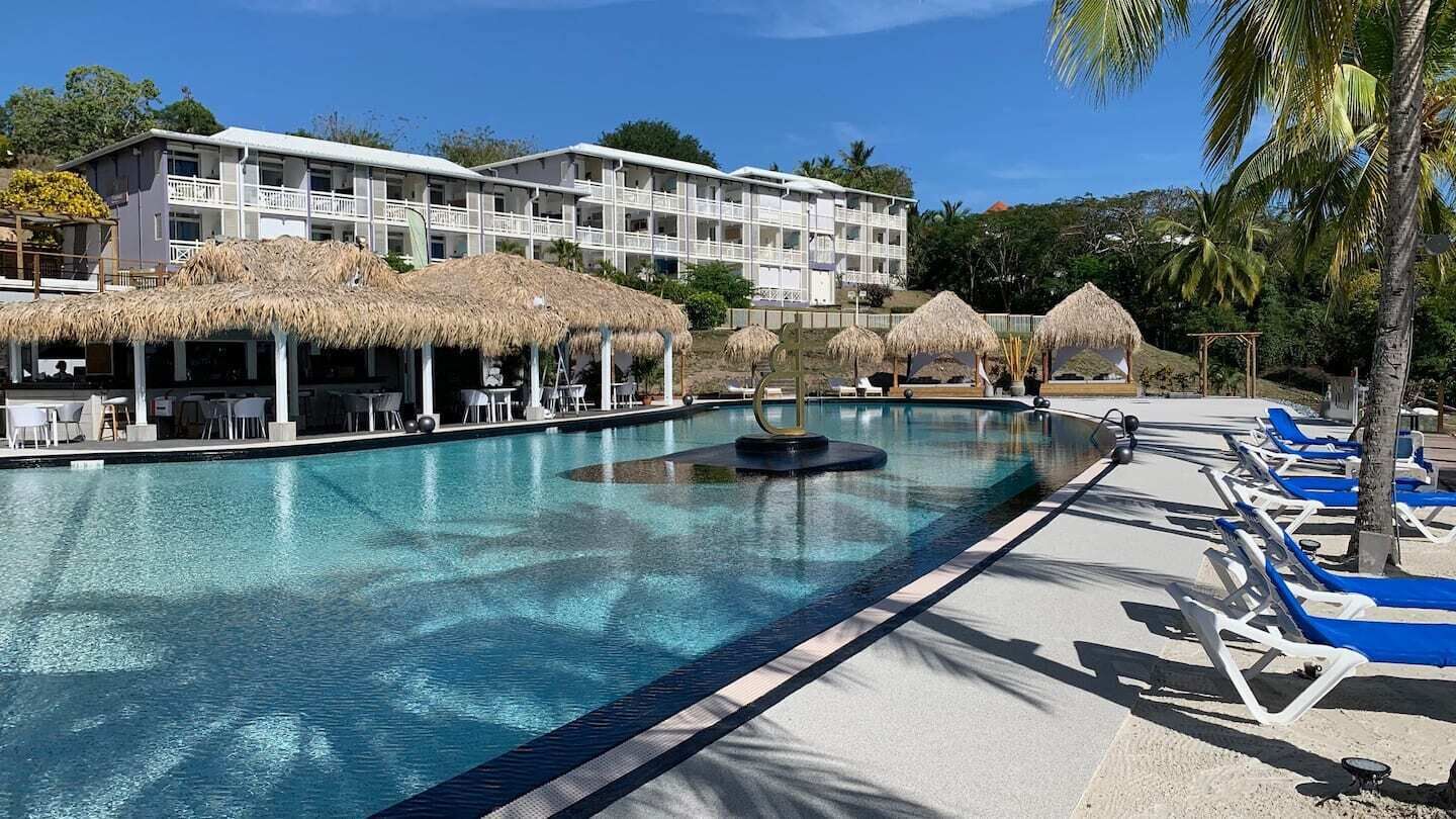 A swimming pool with lounge chairs and thatched umbrellas, surrounded by a building with balconies.