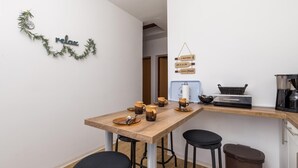 Una cuina compacta amb una taula de fusta, dos tamborets, una cafetera i un cendrer.