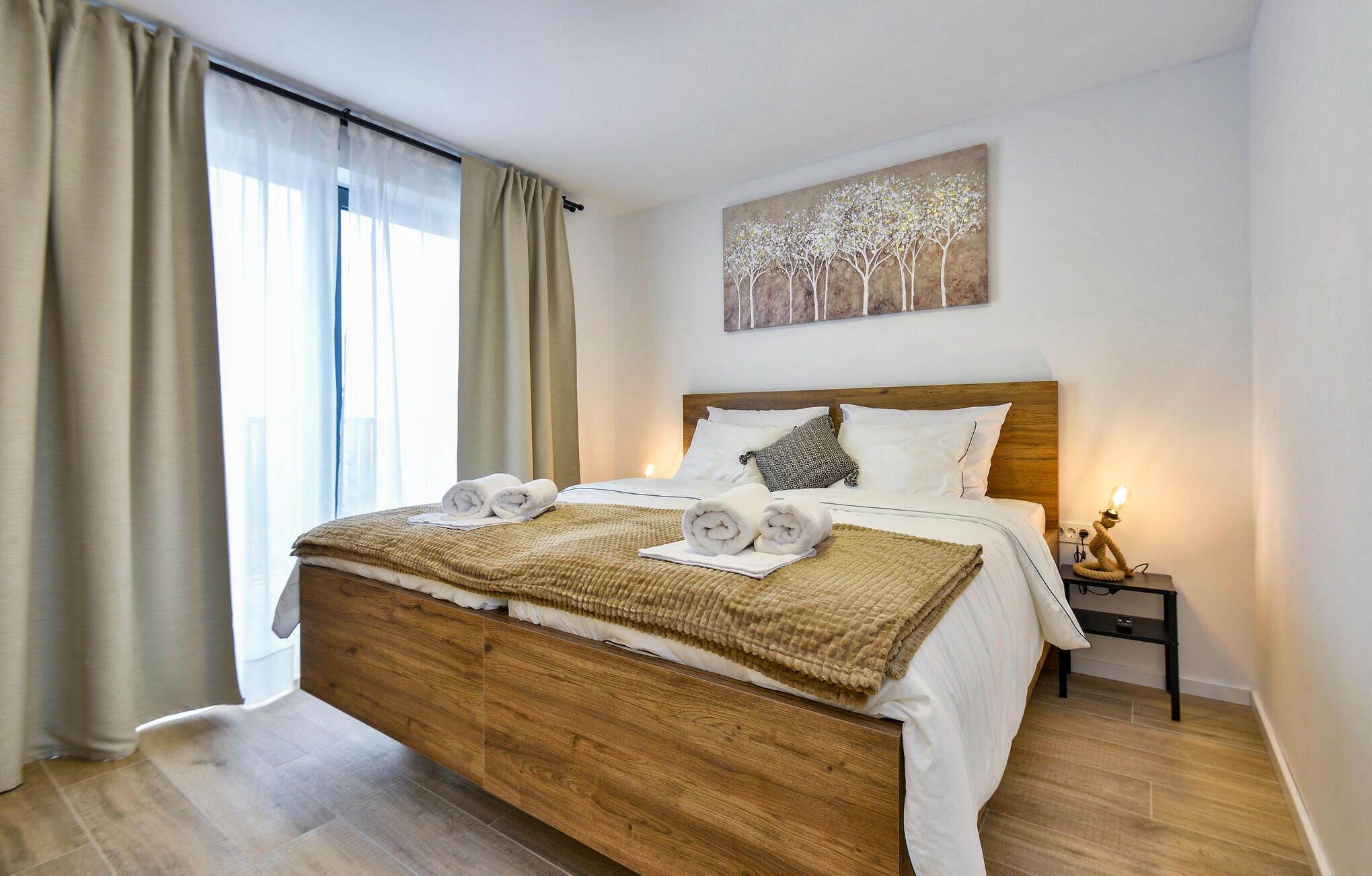 Una camera da letto moderna con un letto in legno, biancheria da letto bianca e un quadro raffigurante alberi al muro.