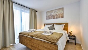 Un dormitorio moderno con una cama de madera, ropa de cama blanca y un cuadro con árboles en la pared.