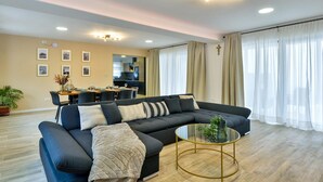 Una sala de estar moderna con un sofá seccional, una mesa de centro de vidrio y un área de comedor al fondo.