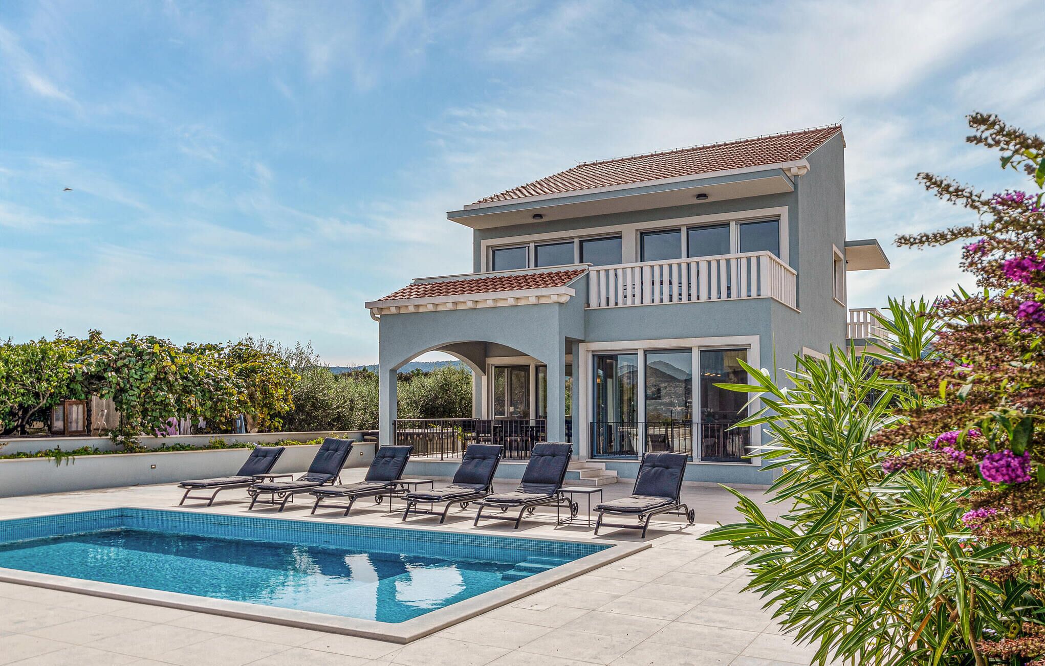 Une maison à deux étages avec une piscine, un espace salon extérieur et un jardin.