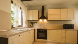 A kitchen with white cabinets, a black range hood, a microwave, and a window with curtains. - Stunning home in Labin (Labin)