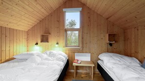 Et hyggeligt værelse med trævægge, to senge, et vindue og et lille bord med en bog.