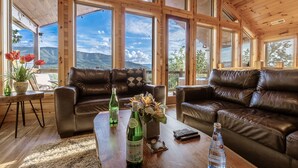 A spacious living room with leather sofas, a wooden coffee table, and large windows offering mountain views.