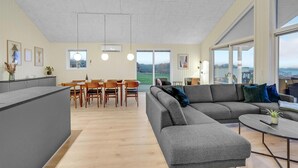 Amplia sala de estar con un sofá gris, una mesa de comedor con sillas y una zona de cocina.