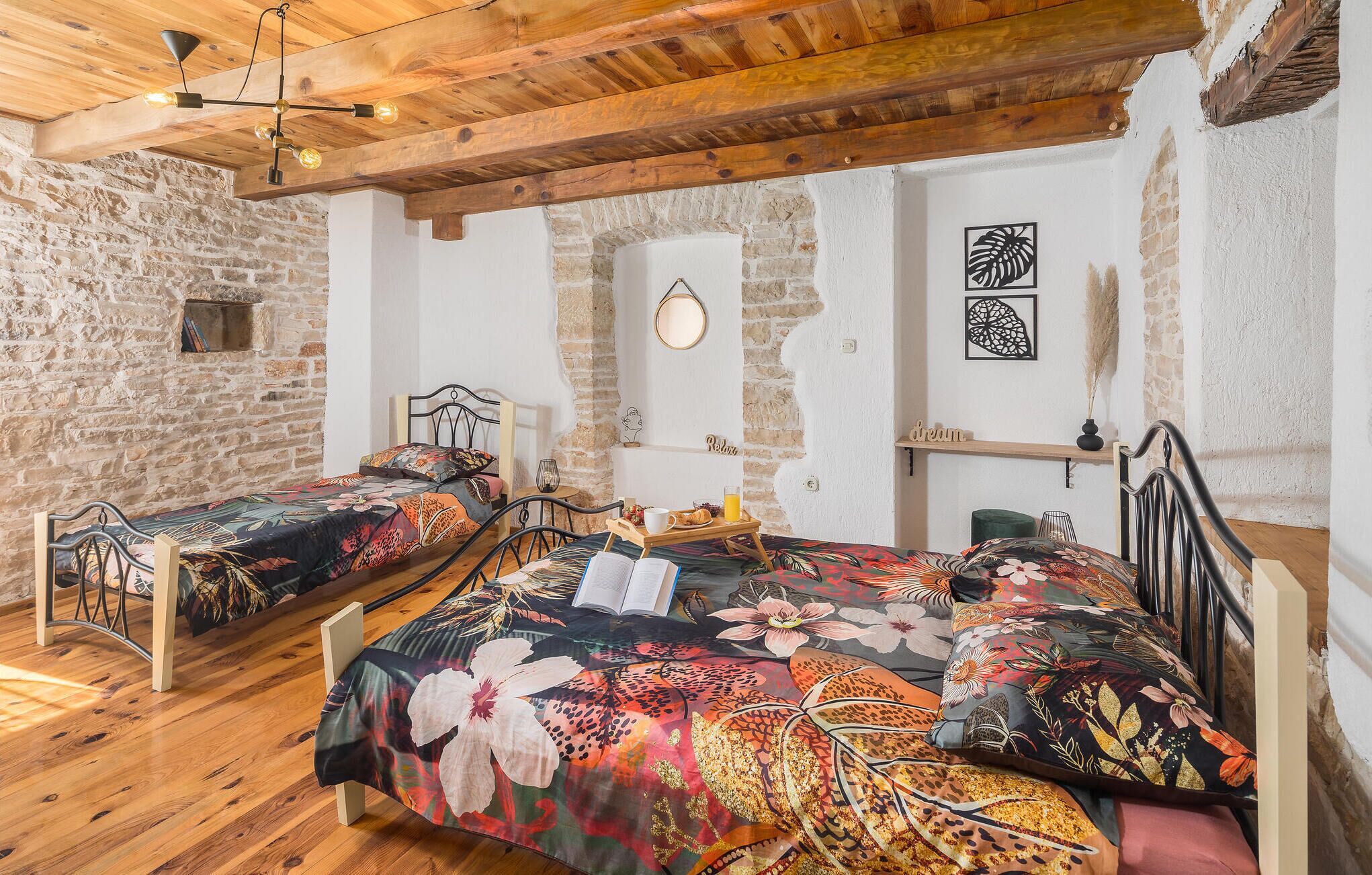 A rustic bedroom with two beds, wooden beams, stone walls, and a small window.